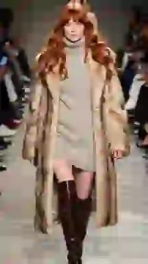 Modella in passerella con un abito maglione beige con una lunga pelliccia e stivali marroni. Opzione vestiti per il cambio vestiti AI.