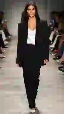 Modella in passerella con un blazer nero su misura con canotta bianca. Opzione vestiti per il cambio vestiti AI.