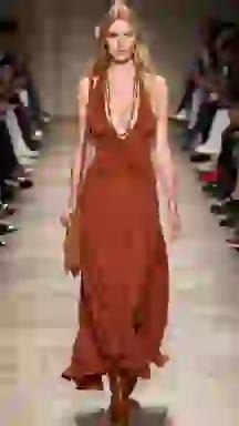 Modella in passerella con un maxi abito in pelle scamosciata color ruggine e frange. Opzione vestiti per il cambio vestiti AI.