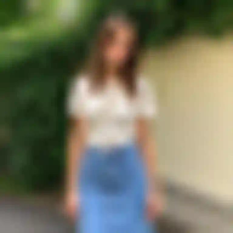 Una donna con una maglietta bianca e una gonna di jeans posa con sicurezza su una strada.