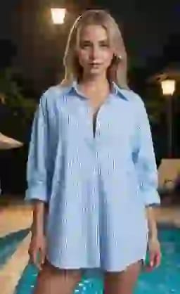 특대 파란색 줄무늬 셔츠를 입은 금발 여성이 수영장 옆에서 포즈를 취하고 있습니다.