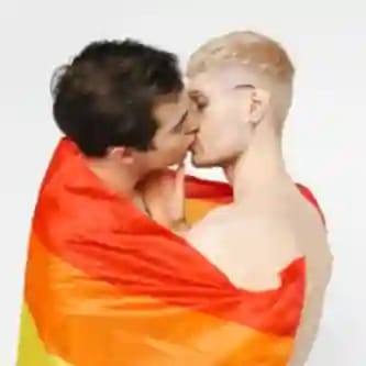 Een homopaar kust hartstochtelijk terwijl ze gehuld zijn in een grote regenboogvlag.