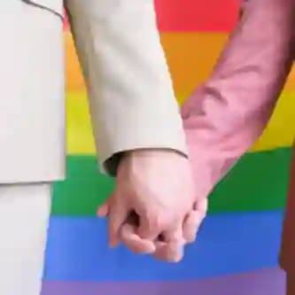 Met elkaar verweven handen tegen een kleurrijke LGBTQ+ regenboogvlagachtergrond.